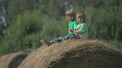 Naklejka na ściany i meble Cute little cheerful kids playing and having fun with hay on a straw bale