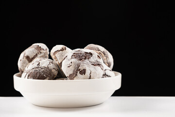 Chocolate chip cookies with cocoa and powdered sugar on a plate on a black background.