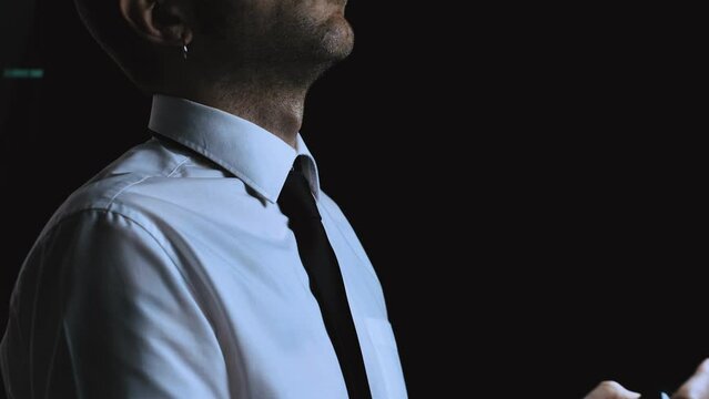 White caucasian male spraying perfume or deodorant on his neck. Handsome business man using fragrance or cologne before a meeting wearing a white shirt and black tie. Dark room background.