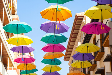 Obraz na płótnie Canvas Street with bright, multi-colored umbrellas against the sky with houses.