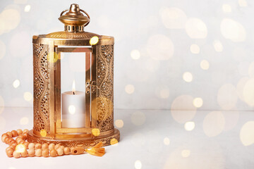 Muslim lantern with glowing candle and tasbih on light background with space for text. Ramadan...