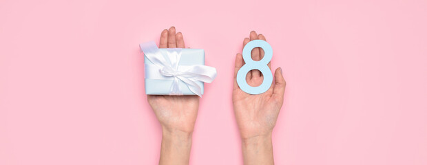 Hands holding gift box and figure 8 on pink background. International Women's Day