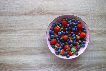 Pink rustic bowl filled with fresh blueberries and strawberries. Wooden background, top view.