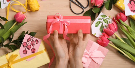 Female hands with gifts and beautiful tulip flowers on wooden background. International Women's Day celebration