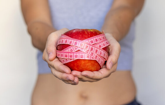 Healthy Food Nutrition For Getting Fit Slim Body Weight Loss.woman Girl Female Hands Holding One Apple Or Pomegranate Fruit And Measure Tape Around Fist.post Partum After Child Birth Belly Recovery