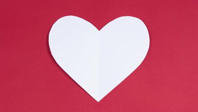 4k Big white heart flaps its wings. Symbol of love. Greeting card. Concept of valentine's holiday, wedding and other occasions to express love. Red background. Looped stop motion animation. Flat lay.