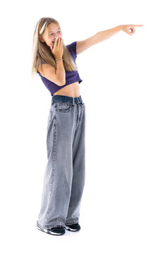 Full length portrait of cute girl in violet T-shirt and blue jeans pointing at side and smiling isolated on white background. Cute female teenager posing in studio.