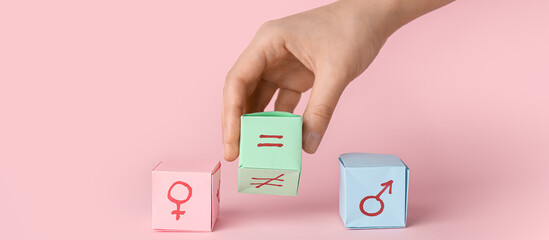 Female hand, paper cubes with symbols of woman and man, equal sign on pink background. Concept of...