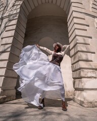 Stylish woman building city. A dancer in a long white skirt dances in front of a building with an...