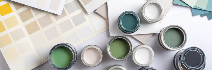 Tiny sample paint cans during house renovation, process of choosing paint for the walls, different green and beige colors, color charts on background