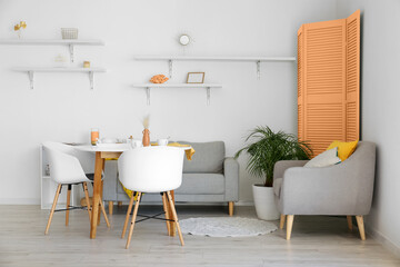 Interior of light dining room with table, grey furniture and orange folding screen