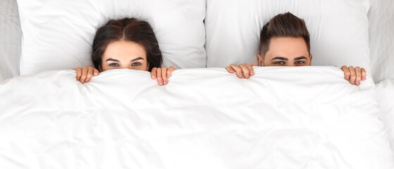 Young couple lying in bed at home, top view