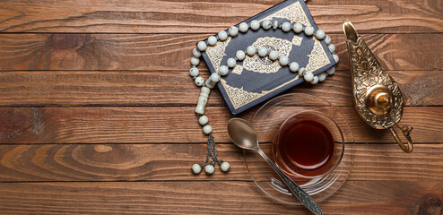 Aladdin lamp, glass of tea, Koran and prayer beads on wooden background with space for text