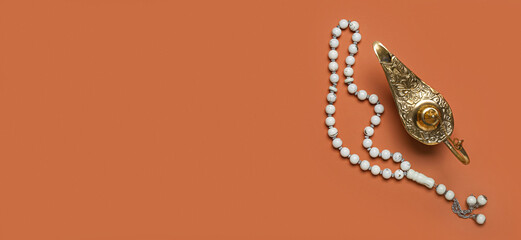 Aladdin lamp of wishes and prayer beads on orange background with space for text