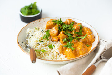 Traditional Indian dish chicken curry with basmati rice and fresh cilantro on rustic white plate on white concrete kitchen table, close up with selective focus. Indian dinner meal - obrazy, fototapety, plakaty
