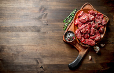 Sliced raw beef on a plate with rosemary and seasonings in a bowl. - obrazy, fototapety, plakaty