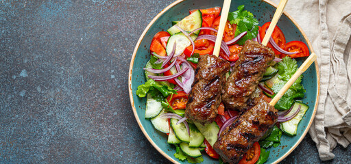 Grilled skewer meat beef kebabs on sticks served with fresh vegetables salad on plate on rustic concrete background from above. Traditional Middle Eastern and Turkish dish Kebab, space for text