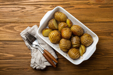 Hasselback potatoes with herbs in white ceramic casserole dish on wooden rustic table background...