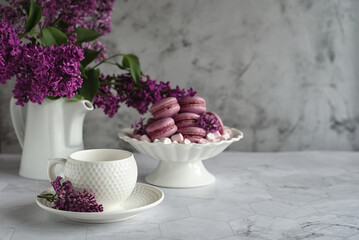 Horizontal spring composition. White coffee pair,  vase with macaroons and a bouquet of lilacs on a light gray background. Festive concept or concept for a good morning wish. Place for text.