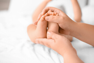 Fototapeta na wymiar Mother massaging her baby's feet in bedroom, closeup