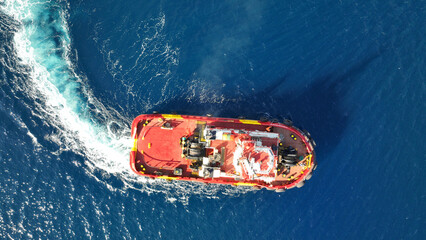 Aerial drone photo of industrial tug assisting boat cruising in deep blue Mediterranean sea