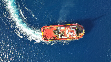 Aerial drone photo of industrial tug assisting boat cruising in deep blue Mediterranean sea