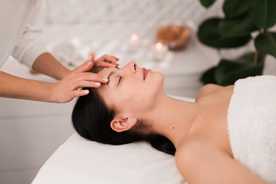 Unrecognizable beautician massaging face of calm female client in salon