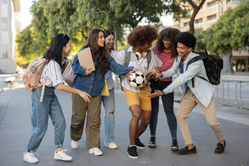 A group of young multi-ethnic students walk through the city on their way to school. They are playing with a soccer ball