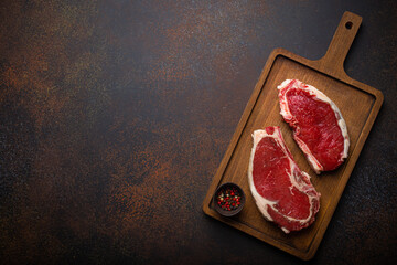 Fototapeta na wymiar Two raw uncooked meat beef rib eye marbled steaks on wooden cutting board with seasonings on dark rustic background ready to be grilled from above, preparing dinner with meat, space for text