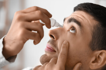 Young man using eye drops at home, closeup