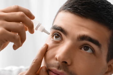 Young man using eye drops at home, closeup