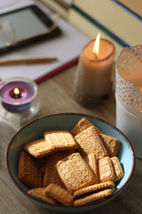 Notebook, pen, tablet, reading glasses, books, phone, candle, bowl of biscuits and cup of tea on the table. Selective focus.