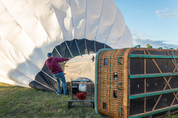 A white, large hot air balloon is being prepared for flight. The team holds the balloon to inflate...