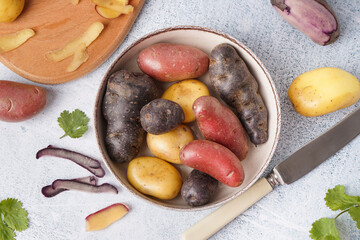 Bowl with different raw potatoes on light background