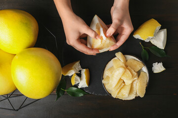 Female hands with piece of sweet pomelo fruit on black background