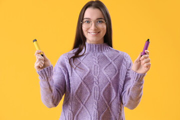 Young woman with disposable electronic cigarettes on yellow background