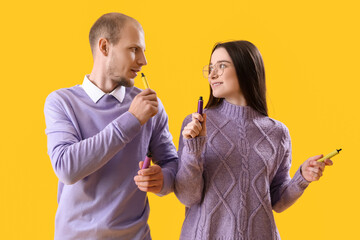 Young couple with disposable electronic cigarettes on yellow background