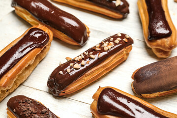 Tasty chocolate eclairs on light wooden background, closeup