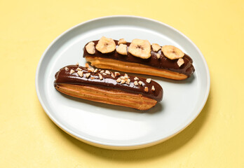 Plate with tasty chocolate eclairs on yellow background