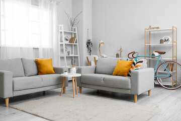 Interior of living room with grey sofas, coffee table, shelving units and bicycle near window