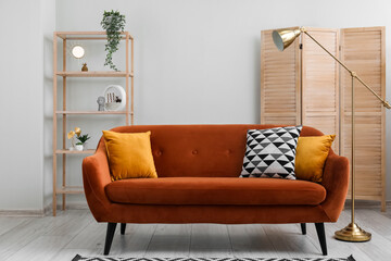 Interior of living room with brown sofa,  shelving unit, wooden folding screen and lamp near grey wall