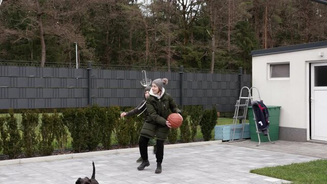Mother and son playing basketball in the backyard with dog looking. in slow motion