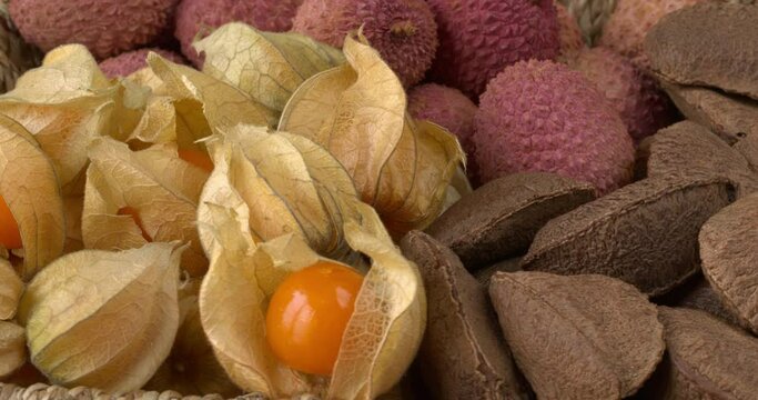 Lychees, Brazil nuts and physalis fruit in braided basket bowl. Table spin.