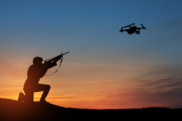 Fototapeta na wymiar Soldier trying to shoot down reconnaissance drone against the backdrop of a sunset. Soldier shoots a quadcopter. Modern methods of warfare. Technology concept.