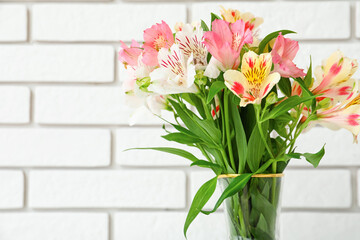 Vase with bouquet of beautiful alstroemeria flowers near light brick wall, closeup. Mother's day celebration