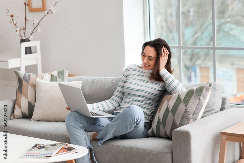 Poster young woman using laptop on grey couch in living room