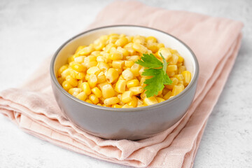 Bowl with canned corn kernels, parsley leaf and napkin on white background