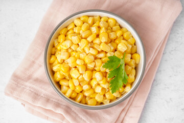Bowl with canned corn kernels, parsley leaf and napkin on white background