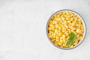 Bowl with canned corn kernels and parsley leaf on white background
