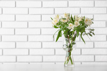 Vase with beautiful alstroemeria flowers on table near light brick wall